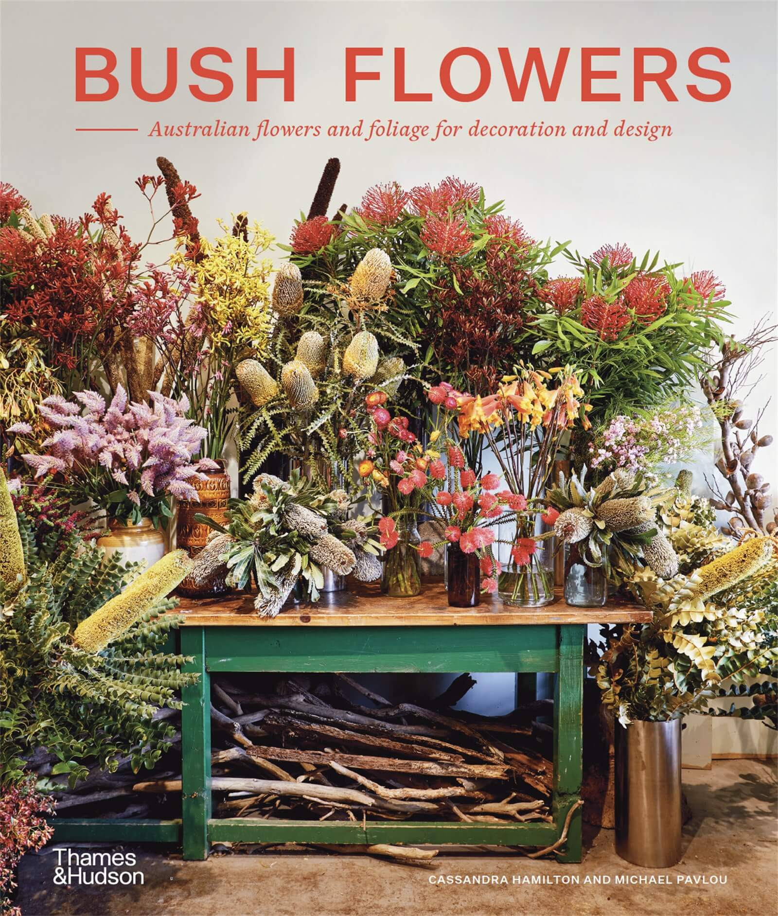 Cover image of Bush Flowers, showing a large array of native australian flowers on green table. Title of Bush Flowers printed in orange, sans serif font, top centre